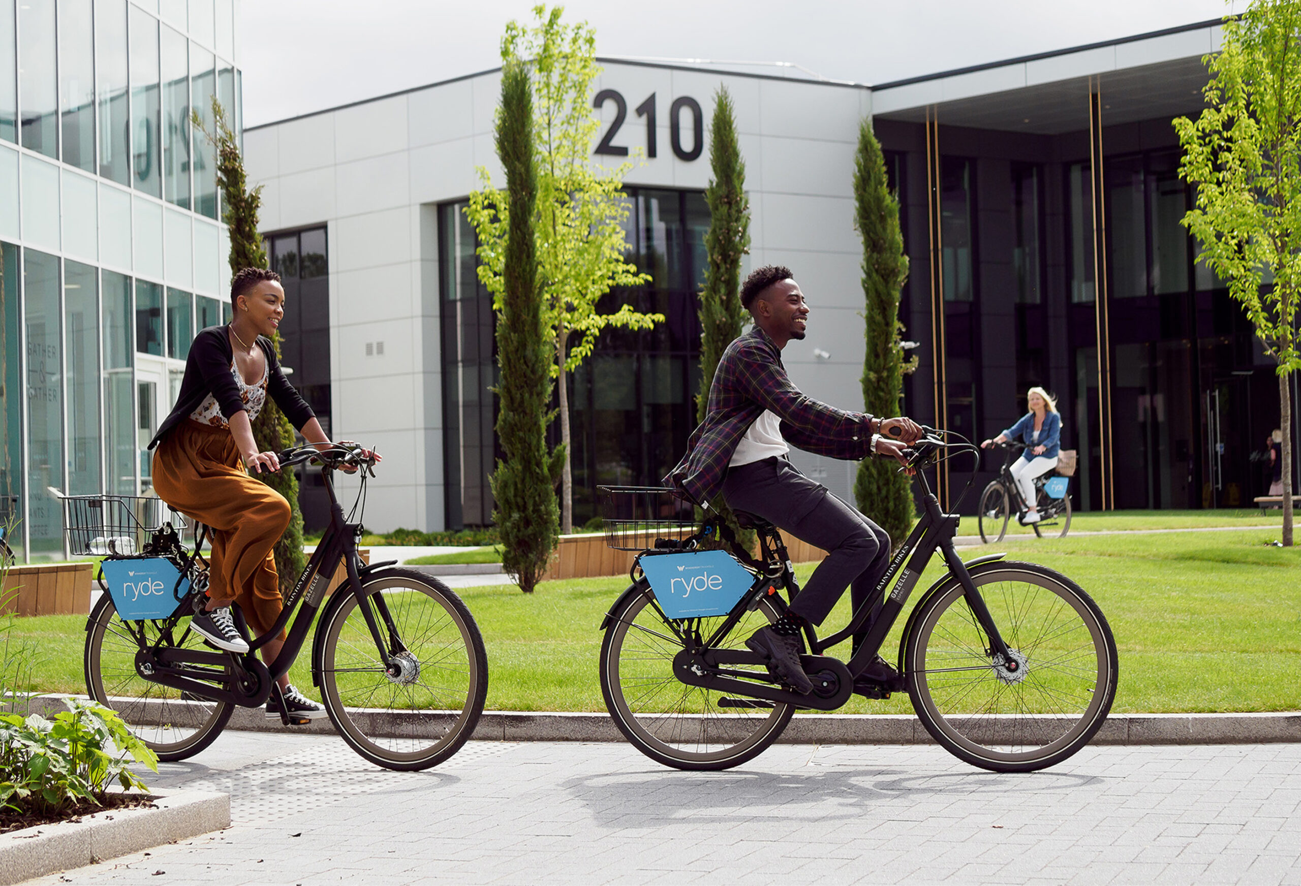 Two happy employees cycling in the sunshine outside at Frasers UK Winnersh Triangle